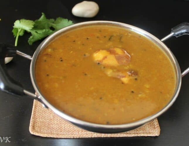 Palakottai Kuzhambu or Jackfruit Seed Sambhar ready and served in a metal bowl with a few sprigs of cilantro in the back