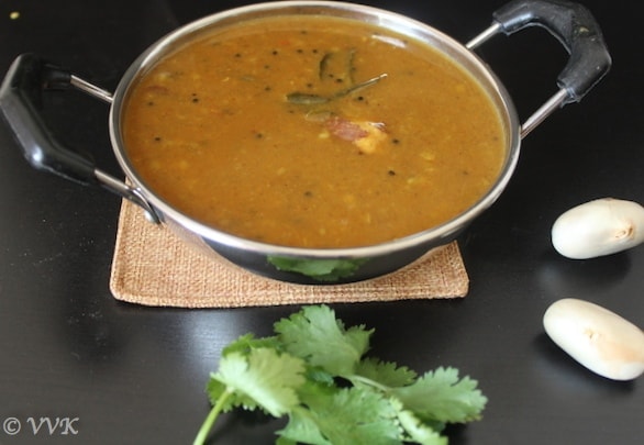 A metal bowl full of the delicious Palakottai Kuzhambu or Jackfruit Seed Sambhar served on a black table