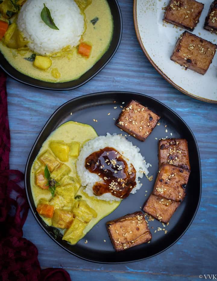 teriyaki tofu on a black plate with rice topped with the sauce and curry on the side