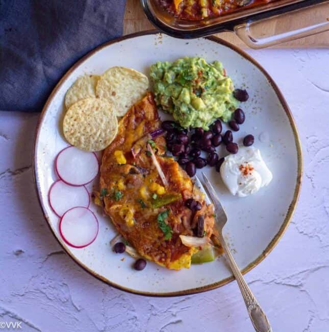 square image of enchiladas served with guac, beans and sour cream