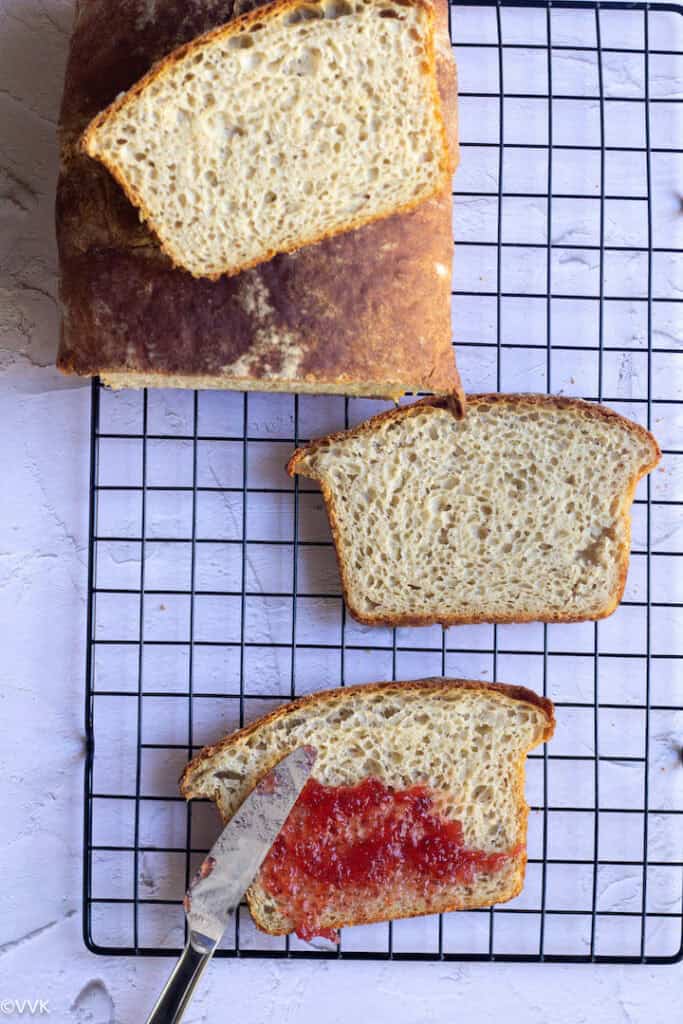 overhead shot of wheat bread loaf with slices on the cooling rack. One slice with jam applied