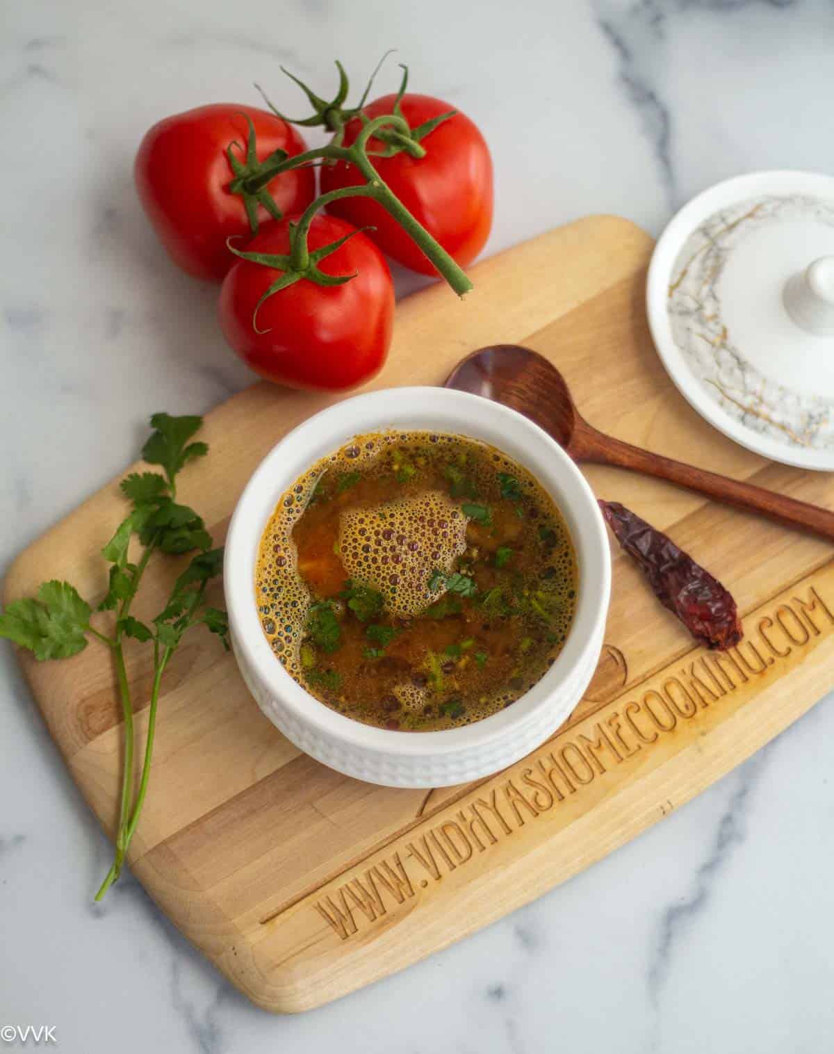 long shot of mysore rasam served in white bowl with tomatoes and cilantro placed on the side