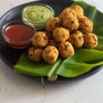 medhu pakoda placed on banana leaf on a black plate with condiments on the side