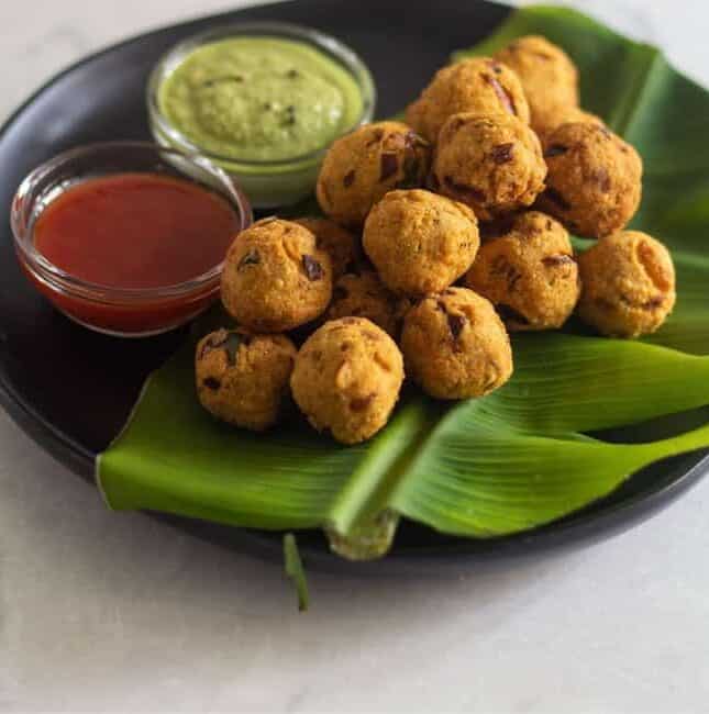 medhu pakoda placed on banana leaf on a black plate with condiments on the side