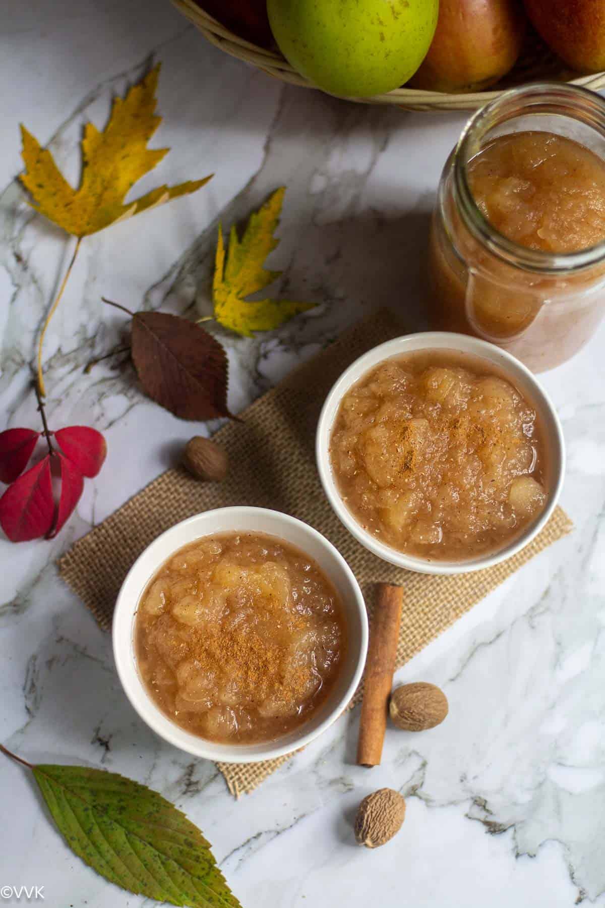 overhead of applesauce in two bowls and glass jar with fall leaves on the side