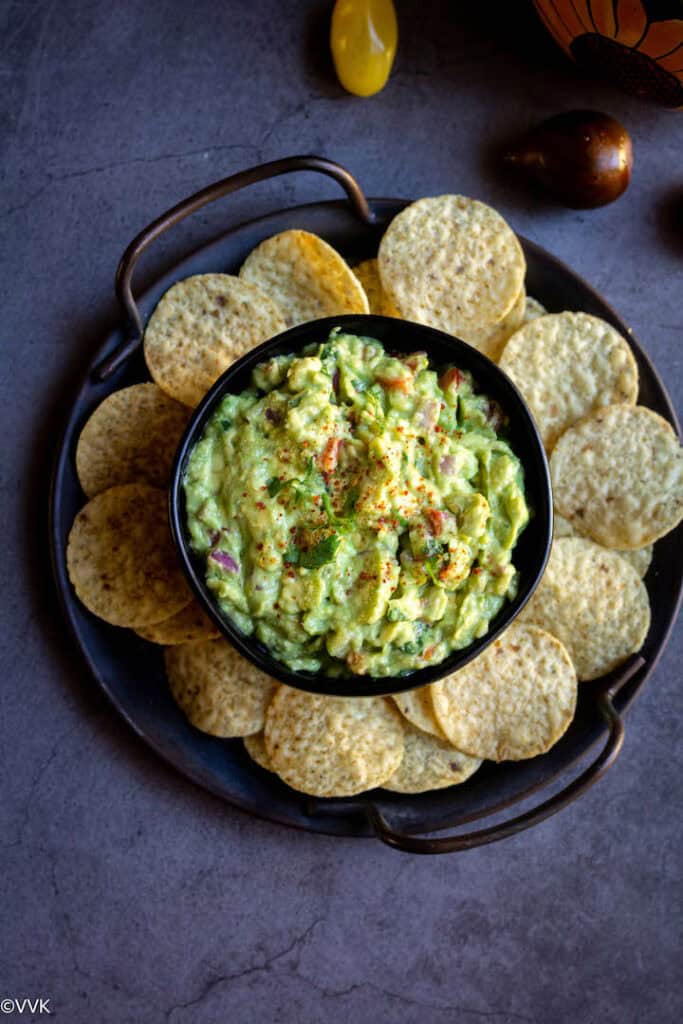 Easy homemade guacamole served in black bowl with chips and with some tomatoes on the side