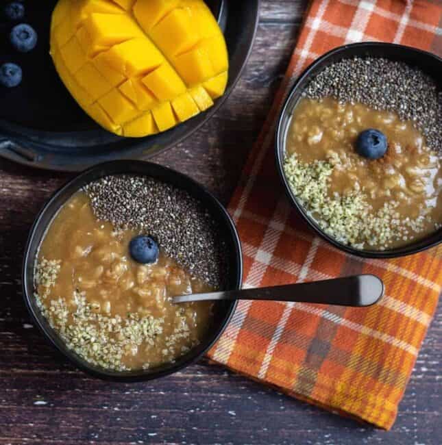 square image of oatmeal served in two black bowls with mangoes on the side