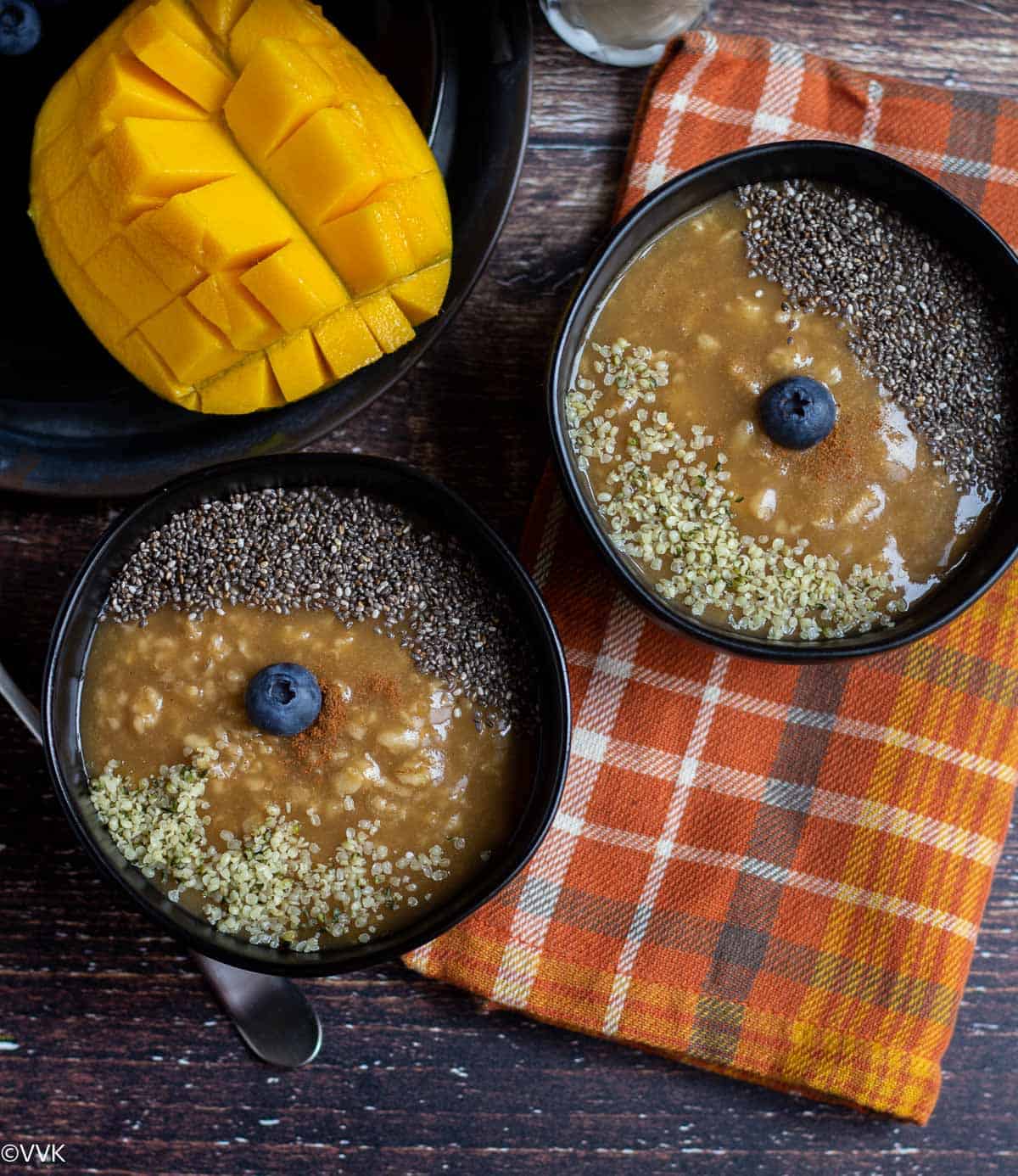 overhead shot of oatmeal served in two black bowls with mangoes on the side