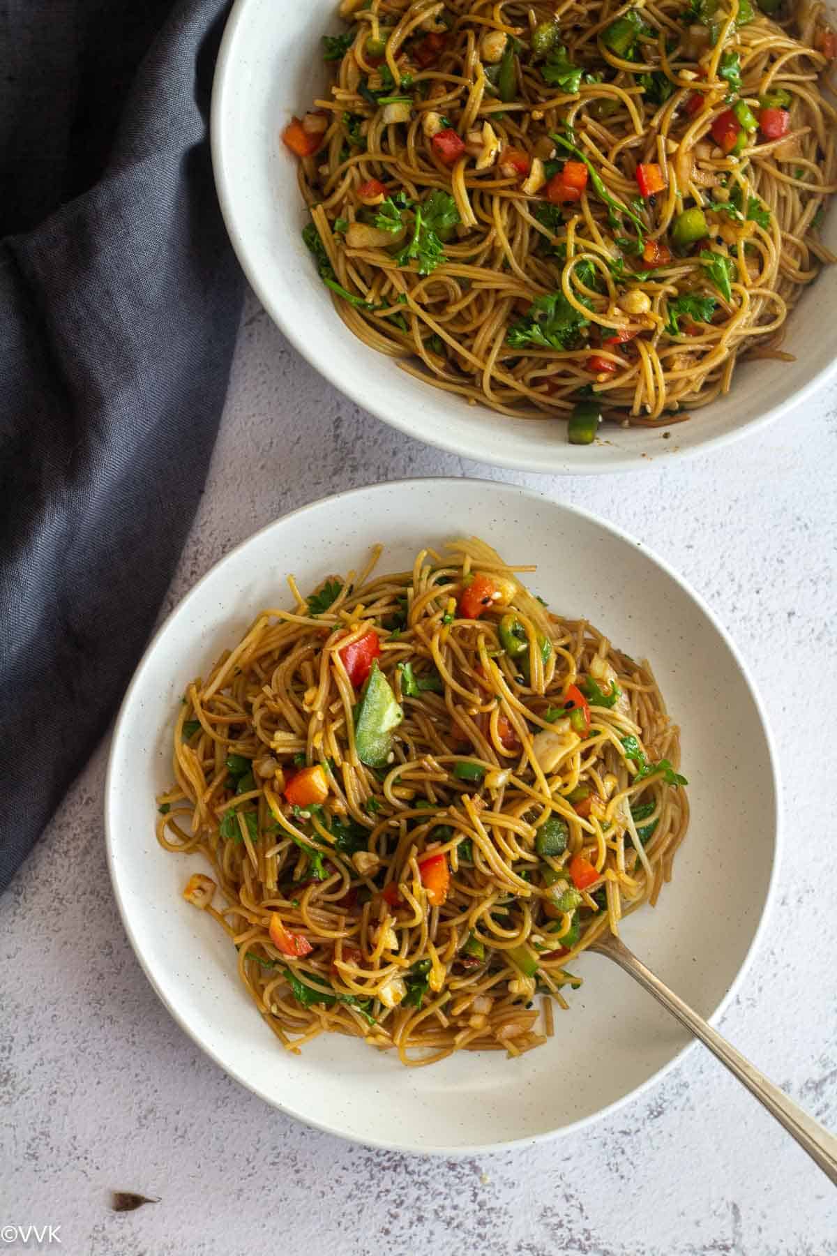 asian noodle salad served in two white plates with gray fabric on the side