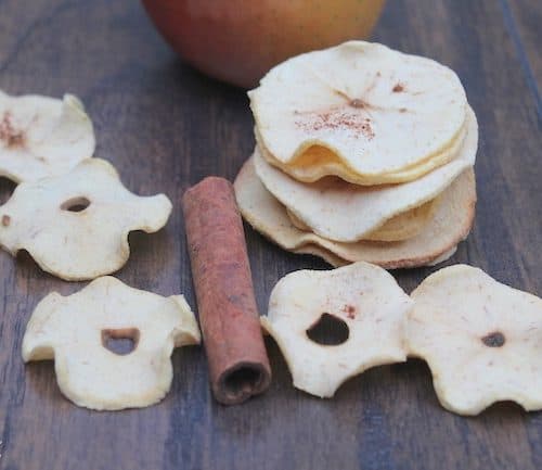 A stack of Baked Apple Chips on a table with an apple and a cinnamon stick among the chips