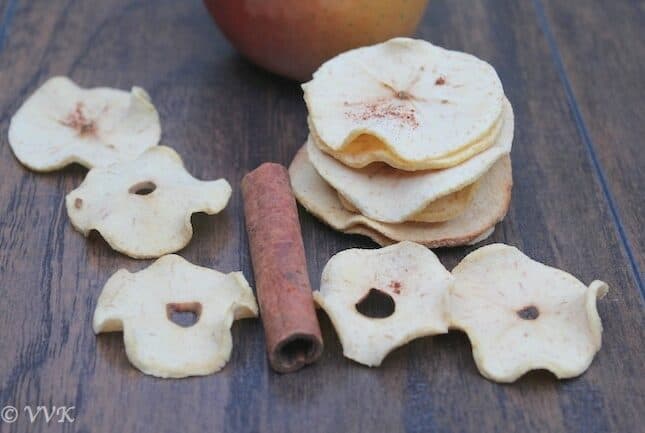 A stack of Baked Apple Chips on a table with an apple and a cinnamon stick among the chips