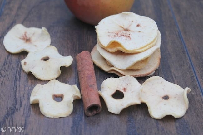 A stack of Baked Apple Chips on a table with an apple and a cinnamon stick among the chips