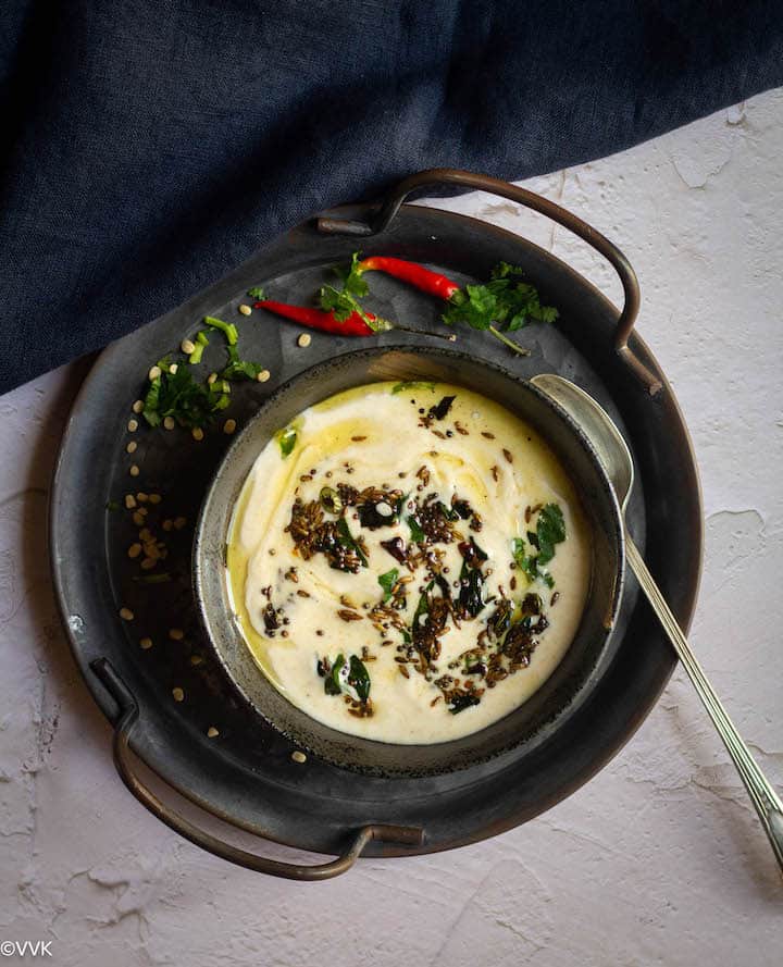 urad dal raita served in black ceramic ware placed on iron tray with chilies and cilantro scattered