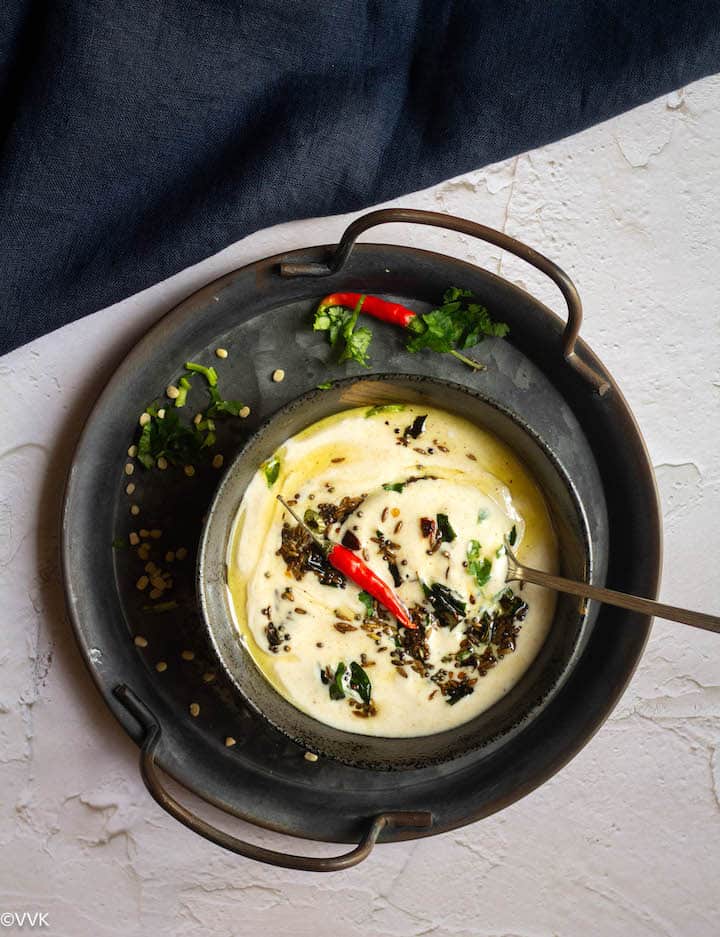 raita served in black serveware with a spoon inside placed on a iron tray