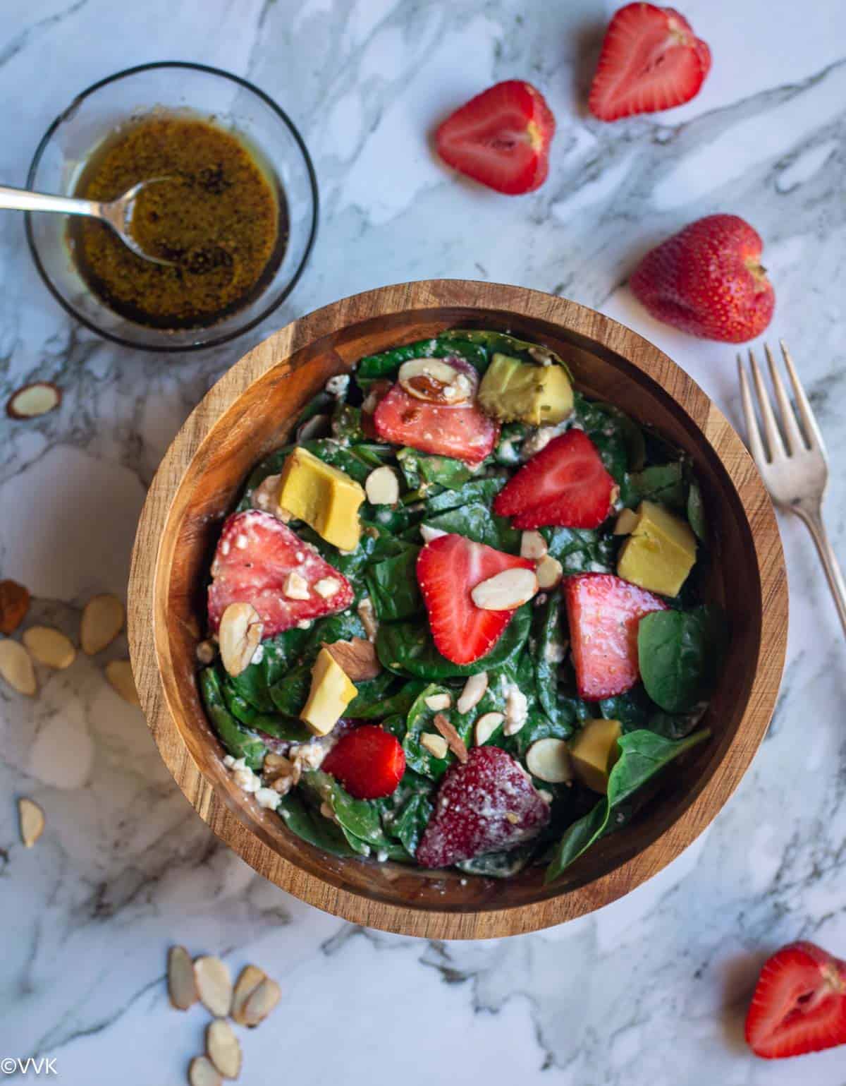 overhead shot of spinach and strawberry salad in a wooden bowl with the dressing on the side