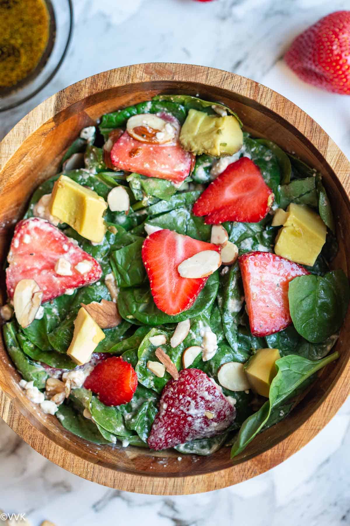 close up shot of spinach strawberry salad with nuts in a wooden bowl