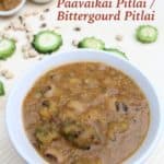 Pavakkai Pitlai or Bitter Gourd Black Eyed Peas Sambar in a white bowl on a light surface with raw ingredients blurred in the back