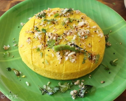 Serving Khaman Dhokla on a big green plate decorated with crumbs and chillies