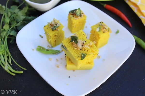 Serving Khaman Dhokla on a big white plate with cilantro and chillies blurred in the background
