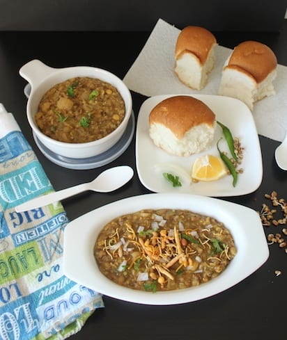 Healthy Missal Pav served in two types of white bowl with bread, lemon and chilis on the side