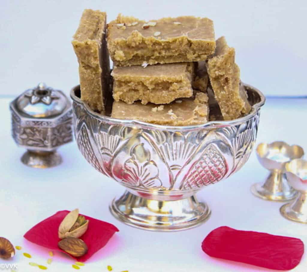 seven cup burfi stacked in silver bowl with rose petals on the side