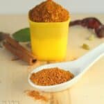 Homemade Chole Masala Powder showcased in a big white spoon with a cinnamon stick and chili blurred in the background