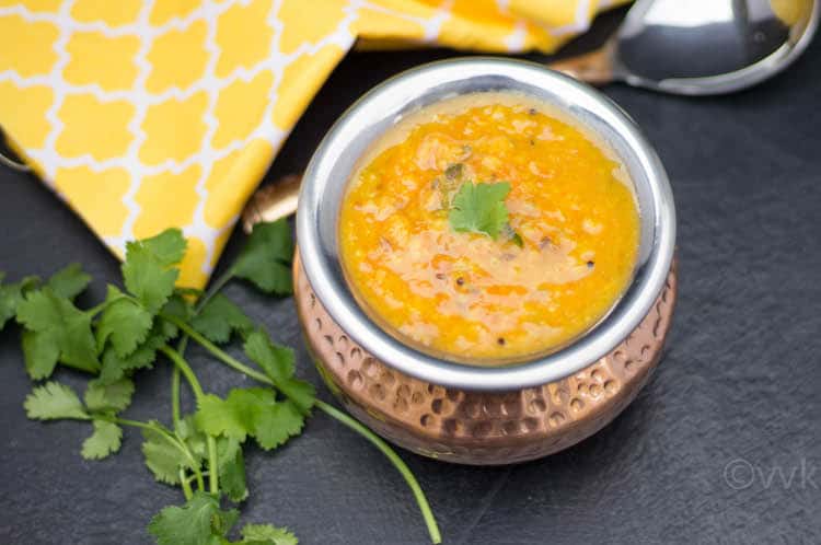 Instant Pot Tomato Pappu served in a bronze bowl with parsley on the side and yellow cloth blurred in the background