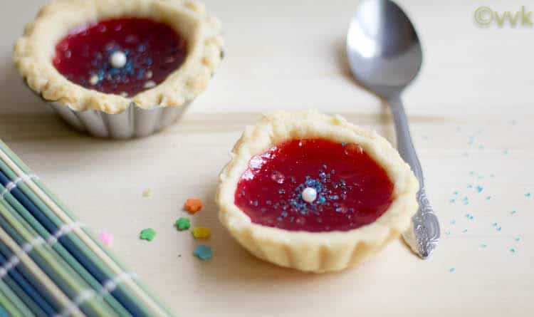 Two delicious Strawberry Jam Tarts with a metal spoon on the right side