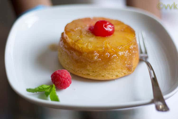 Closeup on the mouthwatering Eggless Single Serving Upside Down Pineapple Cake with a fork and raspberry on the side and a cherry on top
