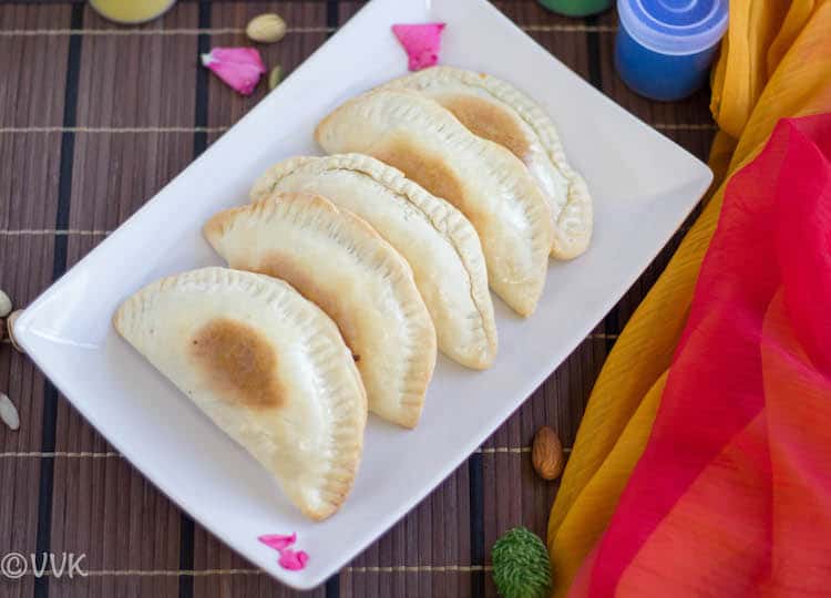Baked Mawa Gujiya served on a white plate and decorated with pink petals