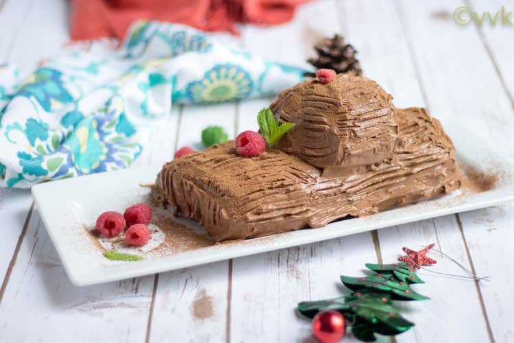 Side view of the Christmas Special Eggless Yule Log Cake in a white tray with lots of raspberries on top and on the sides