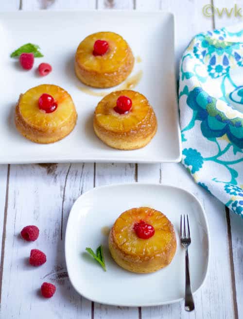 Eggless Single Serving Upside Down Pineapple Cake served on a white plate with plenty of raspberries around it