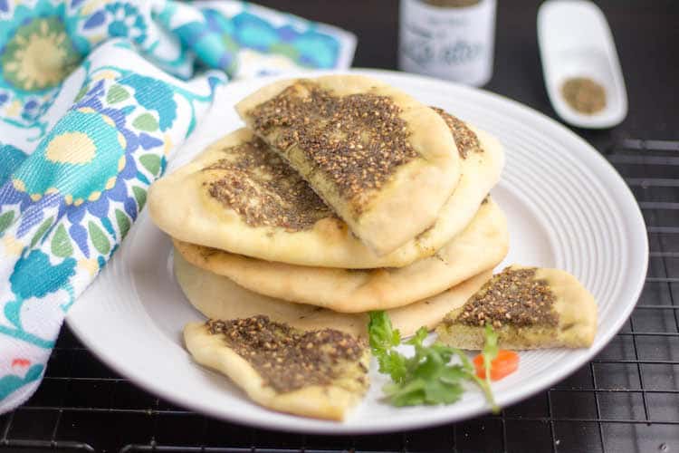 Pita bread topped with zaatar spiced placed on white plate with fabric placed on the side