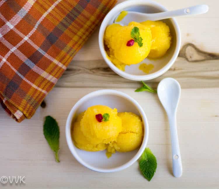 Tropical Sorbet - Mango and Pineapple Sorbet Overhead Shot on the Dish Served in Two White Bowls with Green Leaves and Red Brownish Fabrics Next to It