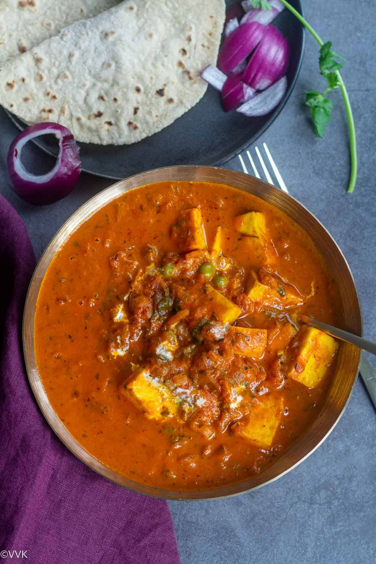 close up overhead shot of paneer curry with pasta sauce served in brassware with roti