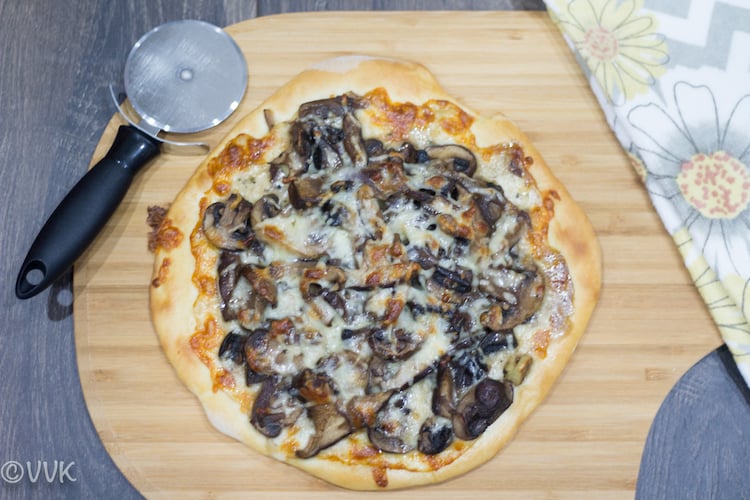 Wild Mushroom Pizza ready to be cut into slices on a wooden board