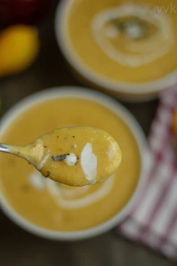 creamy butternut squash soup in a spoon with bowls in a blurry