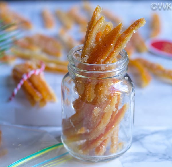 Candied Orange Peels in a jar with more peels blurred in the background