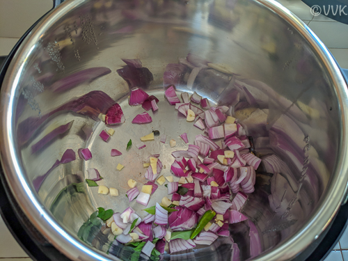 Adding the chopped onion, garlic, ginger, curry leaves, cardamom, cinnamon, and the green chilies