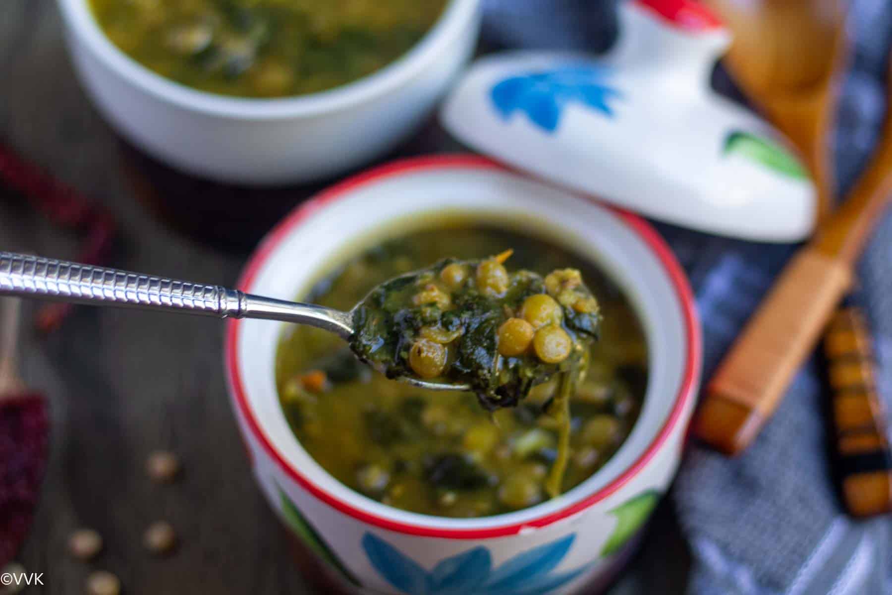 close up shot of vegan dal palak served in a ceramic ware with a spoon lifting the dal