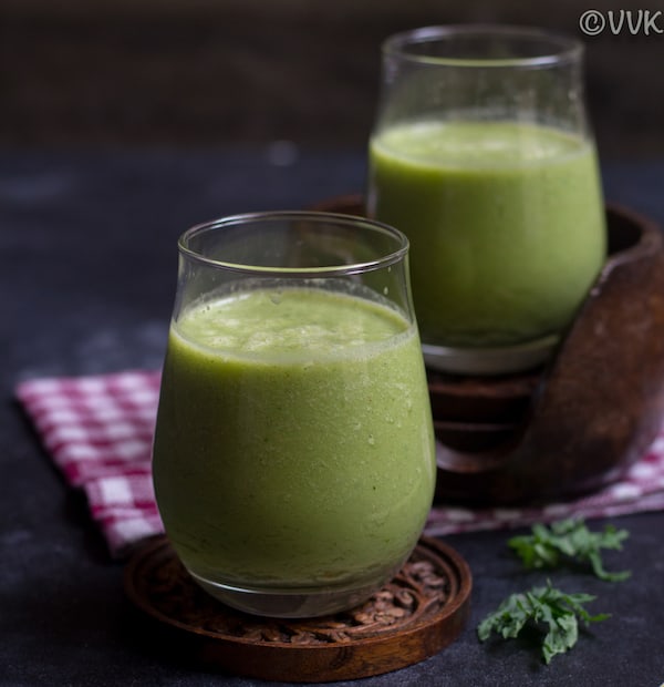 Two glasses of kale smoothie on a wooden coaster