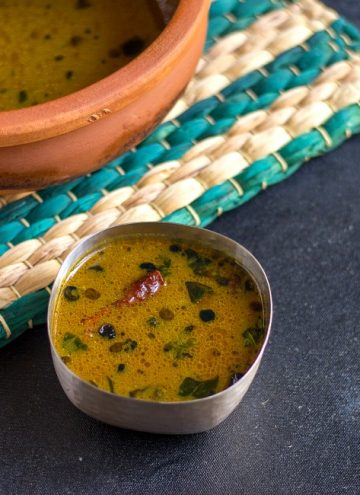 vathal kuzhambu in a small bowl with the claypot behind