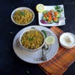 onion biryani in a bowl kept on a plate with raita and raw vegetables