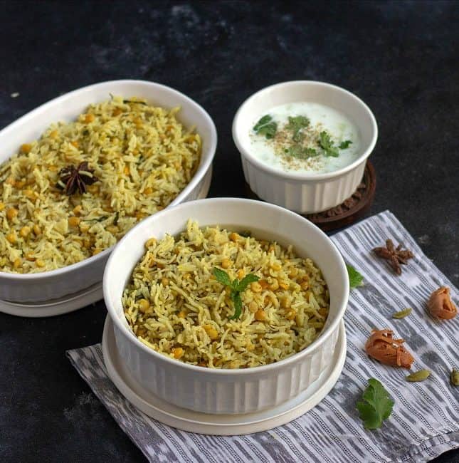 qubooli biryani in white ceramic pot with whole spices on the side
