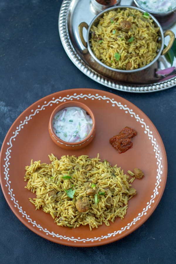 bhatkal biryani in a clay plate with raita and pickle