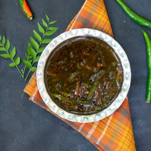 inji puli milagai in a steel bowl with curry leaves on the side