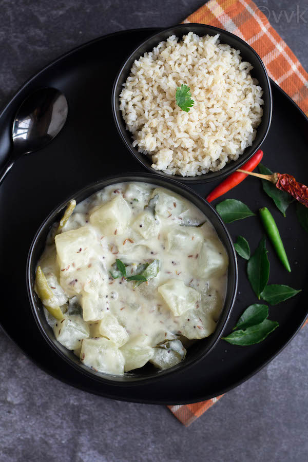 white pumpkin kootu in a black bowl placed on a blackplate with rice on a bowl too