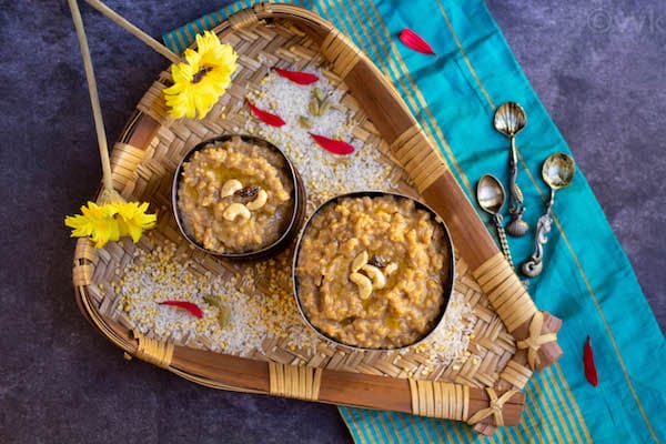 top angle shot of sakkarai pongal in two bowls placed on a muram filled with rice, moong dal and flowers