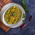 chow chow kootu in a white ceramic bowl with a few curry leaves and red chilies on the side