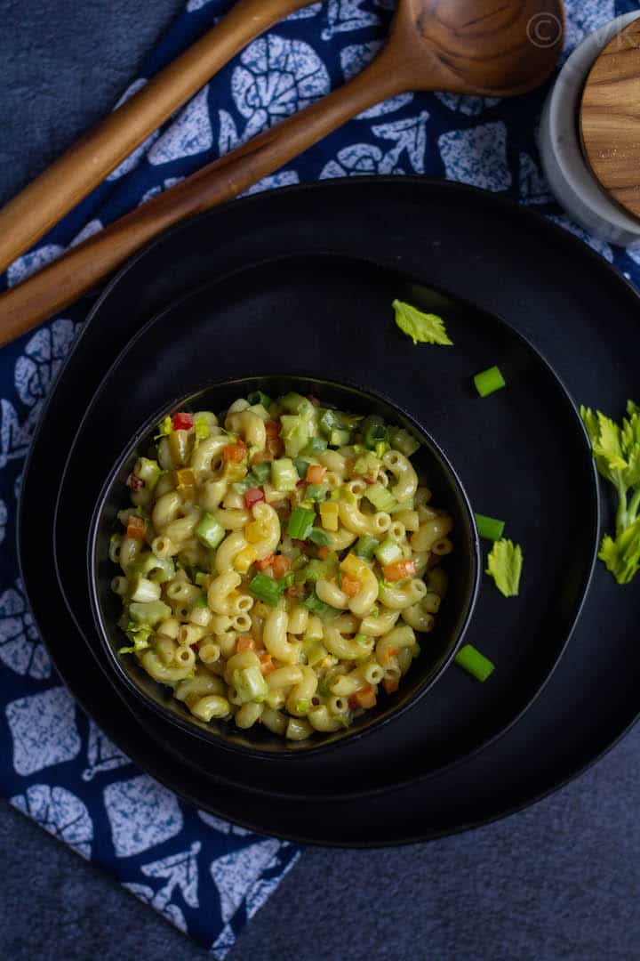 top angle picture of macaroni salad placed in a black bowl on stack of black plates